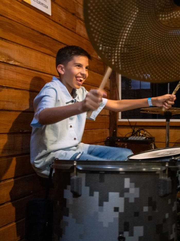 Aluno sorrindo com as baquetas erguidas durante a aula de bateria na Badrumtss