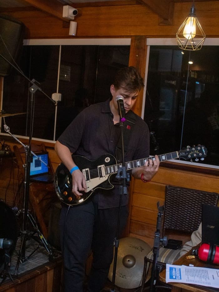 Aluno tocando guitarra e cantando ao microfone na Badrumtss